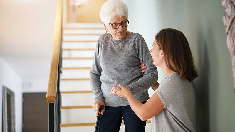 Une auxiliaire de vie aide une personne âgée à descendre les escaliers