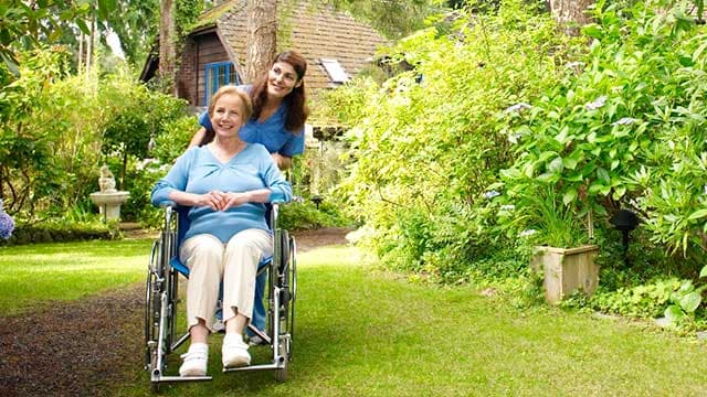 Une auxiliaire de vie accompagne une personne agée dans son jardin